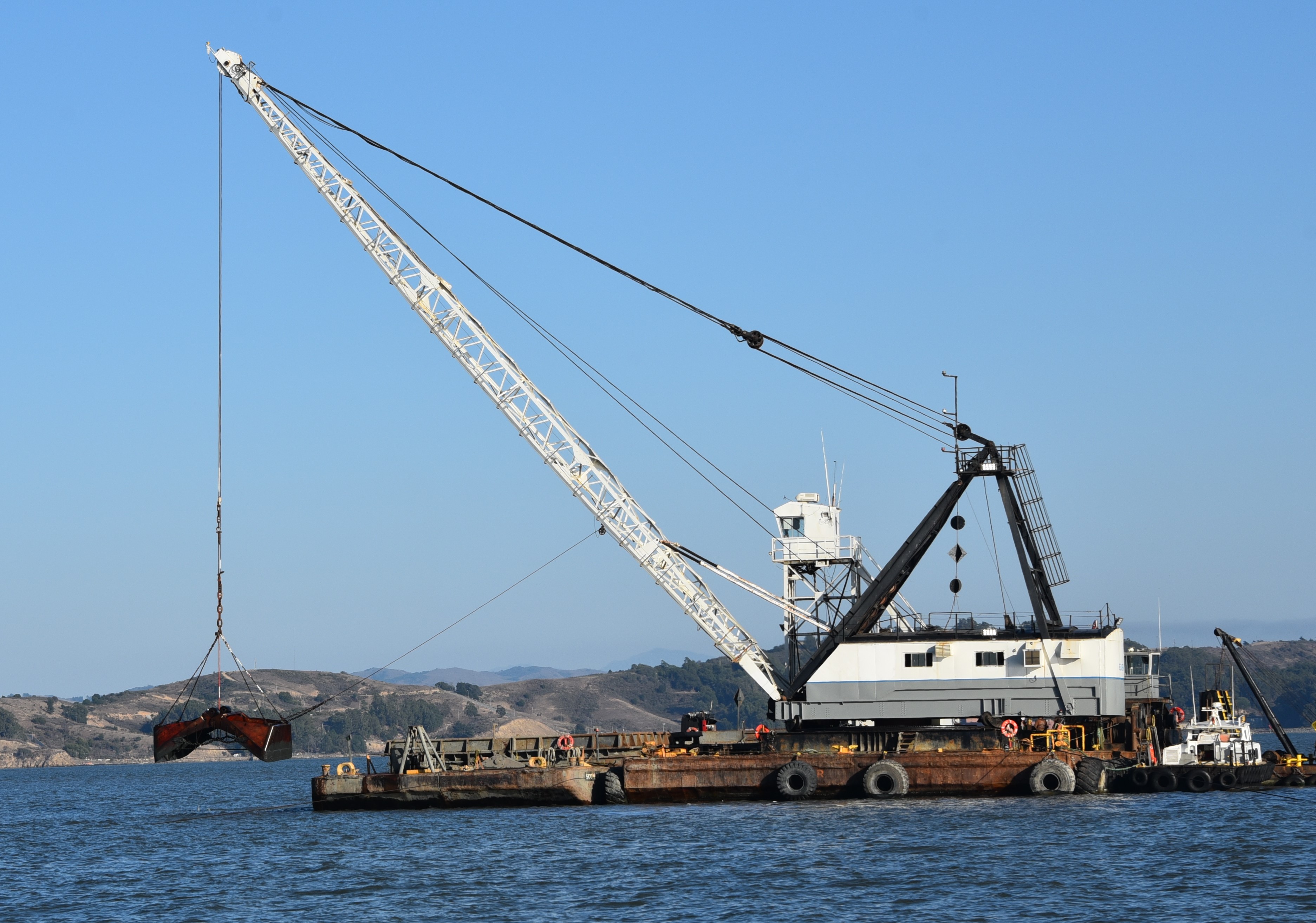 Dredge with open clamshell on the water with hills in the background